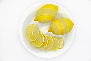 Yellow ripe and juicy fruits of lemons on a white plate. Sliced lemons close-up. Delicious lemons for tea. Lemon slices