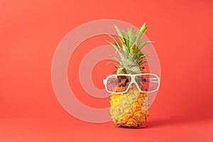 Yellow ripe pineapple in dark sunglasses on a red background. Funny face from a tropical fruit. Concept Copy space.