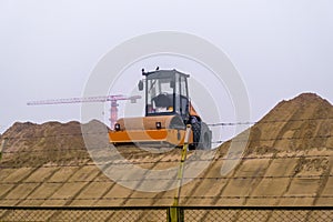 Yellow road compactor on a construction site. Construction equipment on the background of an object under construction