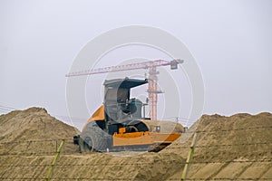 Yellow road compactor on a construction site. Construction equipment on the background of an object under construction