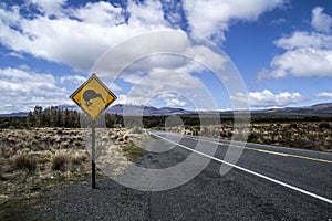 Yellow road sign with kiwi bird crossing by the road. Mountains in the background. Located in the Tongariro National Park, North
