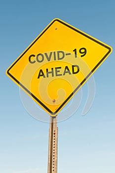 Yellow road sign with text "COVID-19 AHEAD" isolated on a blue background