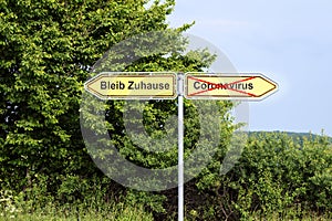 Yellow road signs pointing in opposite directions with German text Bleib Zuhause meaning Stay Home,  and Coronavirus, rural