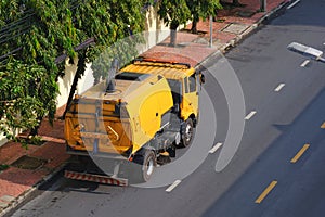 Yellow road sweeper is cleaning on city street in the morning, high angle view from building