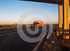 A yellow road train carries cargo against the backdrop of a sunny sunset and blue sky. Concept of work as a truck driver on a