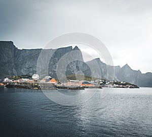 Yellow rorbu houses of Sakrisoy fishing village on a cloudy day with mountains in the background. Lofoten islands