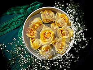 Yellow roses in white bowl on dark green