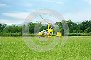 Yellow rotorcraft flying above grass near trees