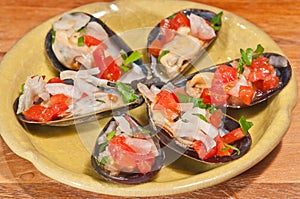 Yellow, round bowl of steamed mussels on half shell with onion, tomato, garlic