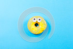 Yellow round donut with eyes on blue background. Flat lay, top view.