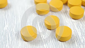 Yellow round vitamin tablets glide and appear slowly on a wooden light table.