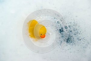 Yellow rubber duck in bath swimming in foam water