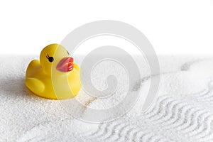 Yellow rubber duck on conceptual white sand in the form of water waves and beach white background