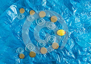 Yellow rubber duck floats on a blue surface through plastic waste pollution. Bottle caps. Polluted environments