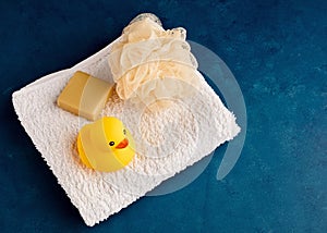 Yellow rubber duck toy with towel, soap and bath puff in the bathroom. Baby or children bathing