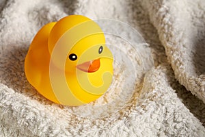 Yellow rubber duck toy on white towel in the bathroom. Baby or child bath time
