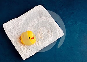 Yellow rubber duck toy on white towel in the bathroom. Baby or child bath time