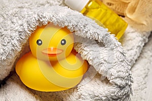 Yellow rubber duck toy wrapped in a white towel in the bathroom. Baby or child bath time