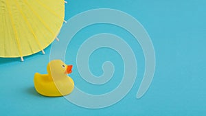 Yellow rubber duck with umbrella on a blue background. Summer vacation trip.