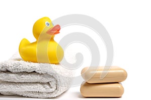 Yellow rubber duckling on white terry towel and two pieces soap