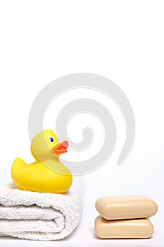 Yellow rubber duckling on white terry towel and two pieces soap