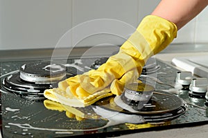 In a yellow rubber glove, a hand cleans a gas stove