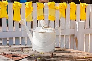 Yellow rubber gloves for work in a garden and a kitchen dry on a white fence and white watering can in the foreground in the summe
