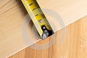 Yellow ruler on the wooden plank in carpenter`s workshop. Selective focus