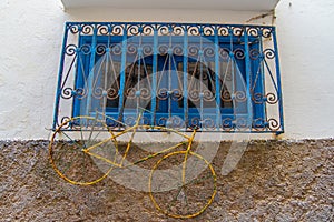 Yellow rusty bicycle hanging on a blue window with iron grating