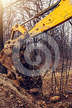 A yellow rusty industrial excavator with a bucket lying on the ground, digging the ground at a construction site in a pond forest