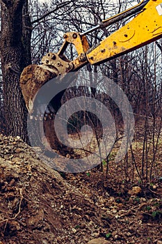 A yellow rusty industrial excavator with a bucket lying on the ground, digging the ground at a construction site in a pond forest