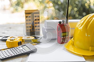 yellow safety helmet and rolled up architectural blueprints on a wooden desk