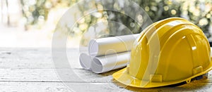 yellow safety helmet and rolled up architectural blueprints on a wooden desk