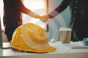Yellow safety helmet on workplace desk with construction worker team hands shaking