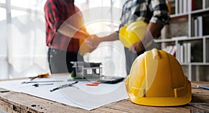 Yellow safety helmet on workplace desk with construction worker team hands shaking greeting start up plan new project