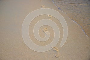 Yellow sand beach with foot step marks and seawater. Lonely traveler barefoot steps. Still seawater on sand beach