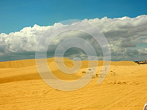 Yellow sand dunes under blue sky with white clouds