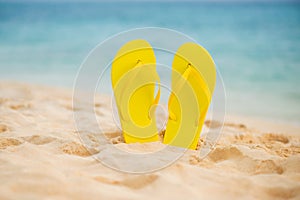 Yellow sandal flip flop on the white sand beach with blue sea and sky background in summer vacations copy space