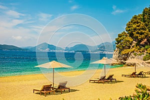 Yellow sandy beach with sun loungers on a Sunny day. Mountain peaks visible in the distance. Beautiful sea background.