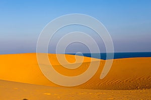 Yellow sandy wavy dunes with blue sea at background