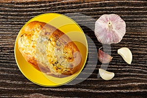 Yellow saucer with garlic bun, head of garlic, slices of garlic on table. Top view