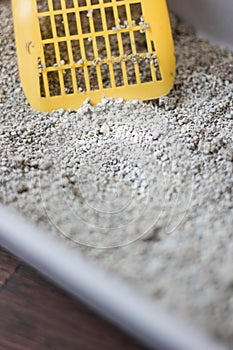 Yellow scoop standing on the litter sand on the litterbox.