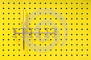 Yellow screwdriver sits in a rack on pegboard photo