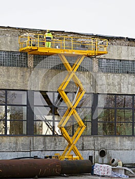 Yellow self propelled scissor lift in action with worker in uniform and safety protective equipment