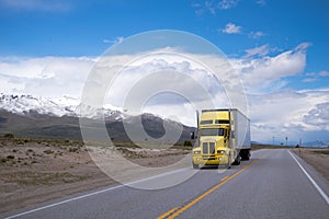 Yellow semi truck with trailer on road with snowy mountain