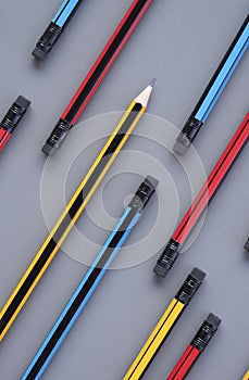 Yellow sharp pencil tip in group of many pencil eraser heads on gray background in vertical frame for background design, concept