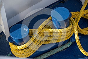 Yellow ship rope tied around blue mooring bollards on a boat deck