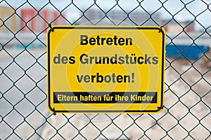 Yellow sign on fence saying: Entering the property prohibited. Parents are responsible for their children german: Betreten des