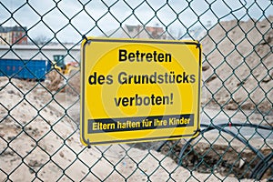 Yellow sign on fence saying: Entering the property prohibited. Parents are responsible for their children german: Betreten des