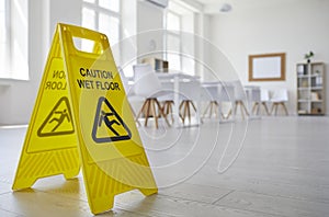 Yellow sign with the inscription Caution Wet Floor which was put in the office after cleaning.